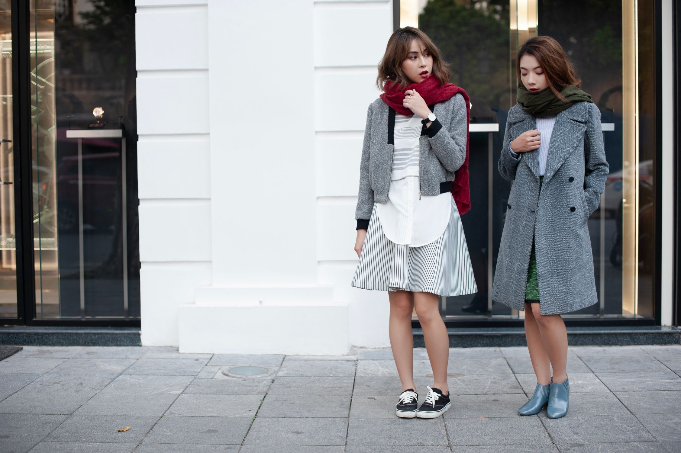 Two friends in coats and scarves outside a city storefront